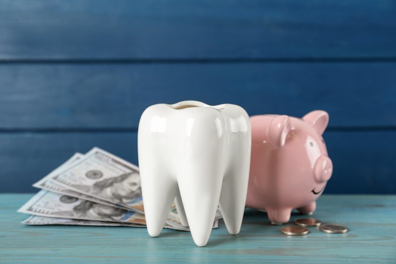 A large model tooth next to a piggy bank and some money